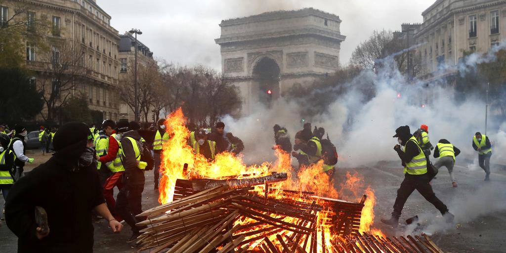 燃え上がる炎のそばを走るデモ隊＝１日、仏パリのエトワール凱旋門近く（ＡＰ）
