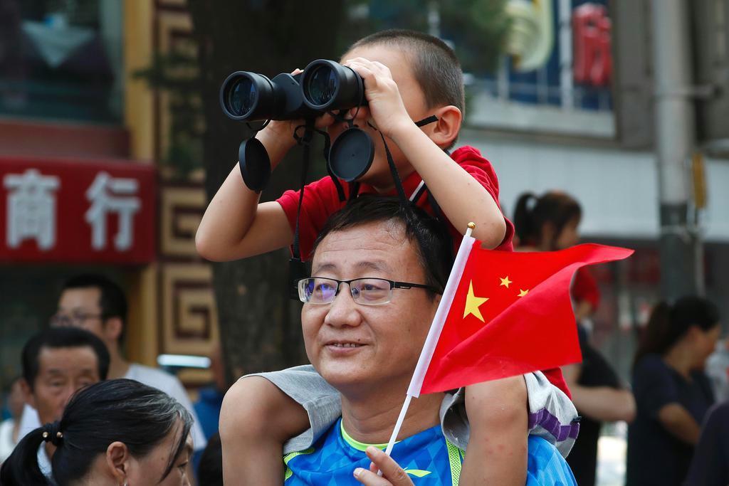 建国70年の記念日に中国国旗を手に軍事パレードを眺める親子連れ。中国共産党は国民の愛国心を高めようと躍起になっている =10月1日、北京(AP)