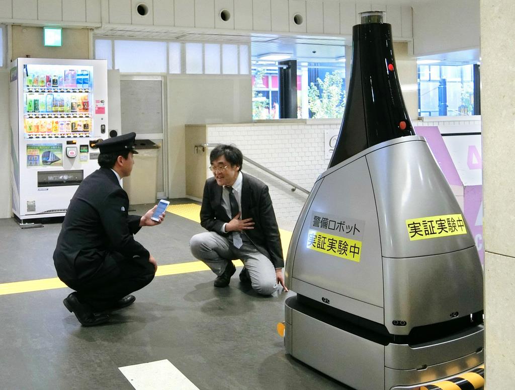 昨年１１月に行われた警備ロボット「ペルセウスボット」の実証実験。不自然な動作から急病人（右奥）を発見し、通報して駅員を呼んだ＝東京都新宿区の西武新宿駅