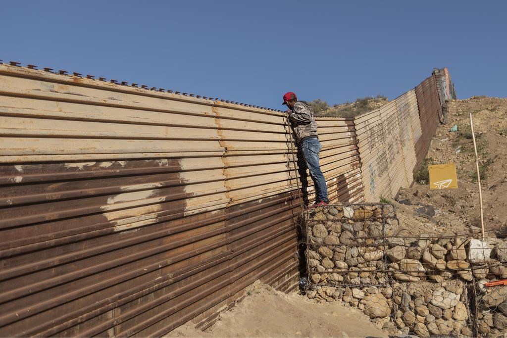 米メキシコ国境のメキシコ側で、フェンスから顔を出し、米国側をのぞき込む移民希望者=1月3日(AP)