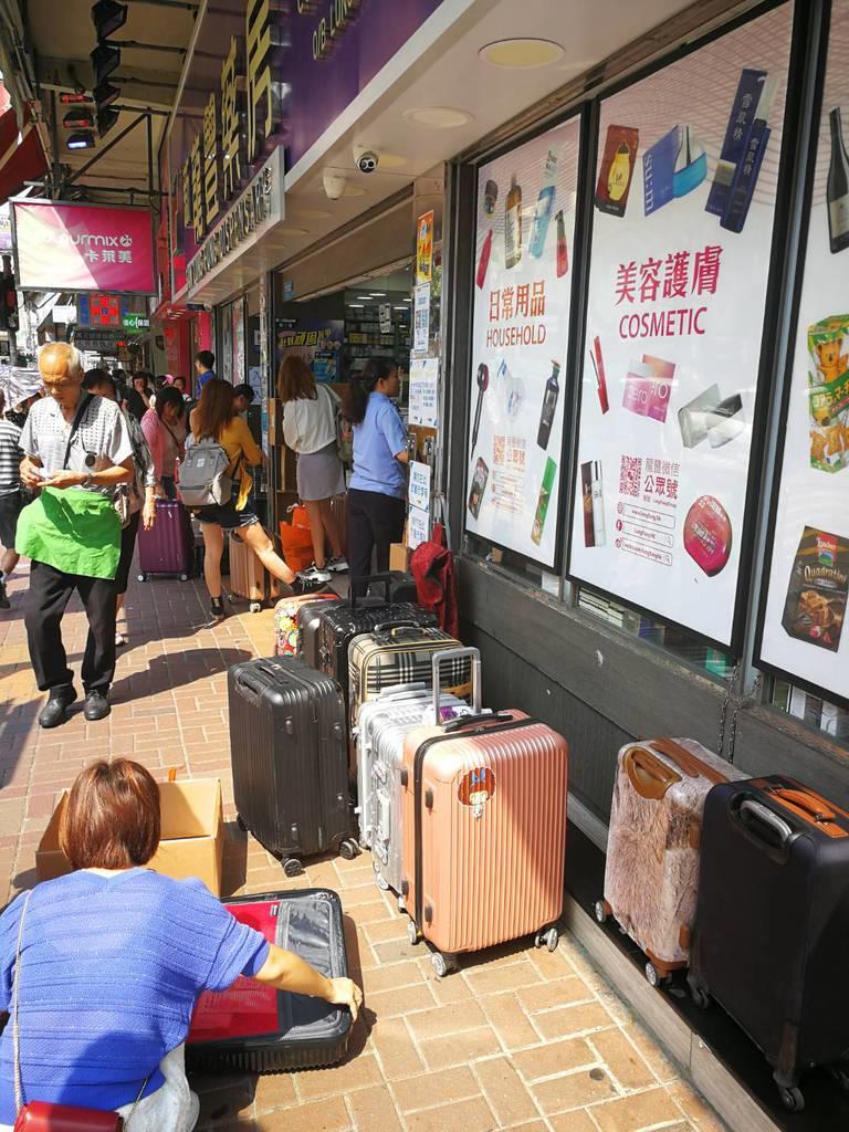 香港北部・上水で、中国に運ぶため購入した商品を荷物に詰め込む客。店の前には客が持ってきたスーツケースがずらりと並ぶ(森浩撮影)