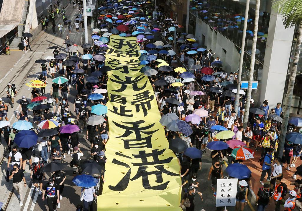 香港で「覆面禁止法」の施行などに抗議し、スローガンを掲げて通りを歩く人たち=5日(共同)