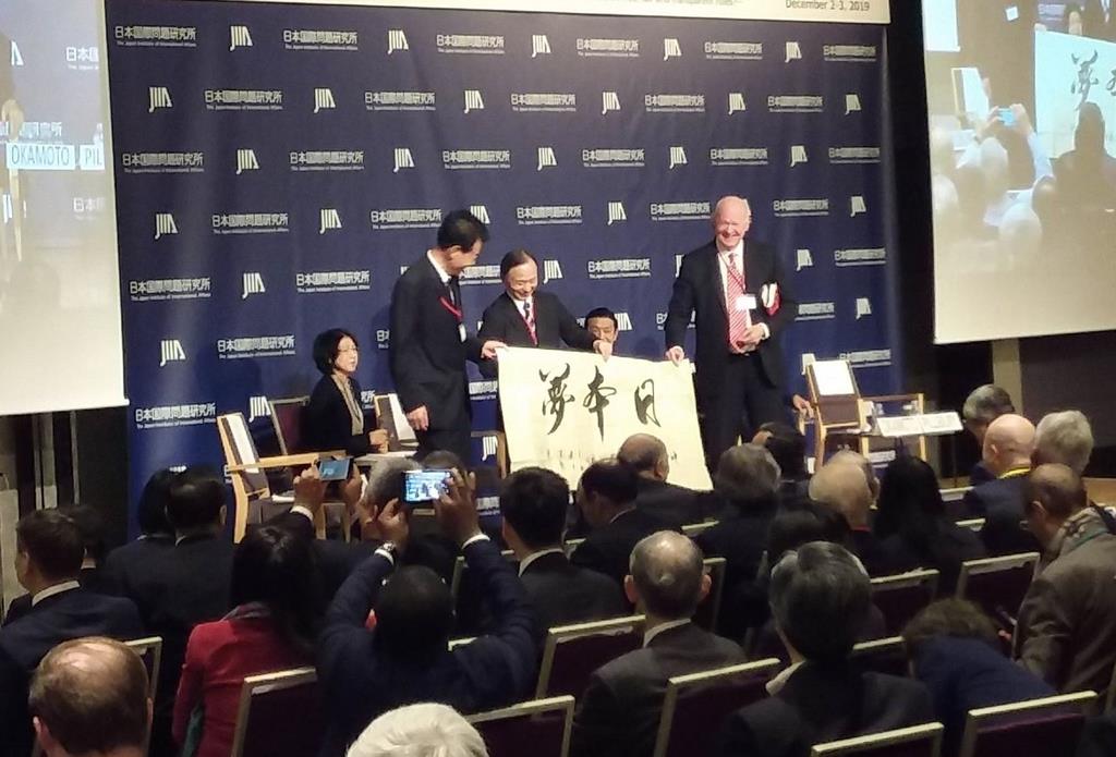 日本国際問題研究所のシンポジウムで持参した幕を掲げる劉明福氏(中央左)と、マイケル・ピルズベリー氏(同右)=12月2日、東京都内