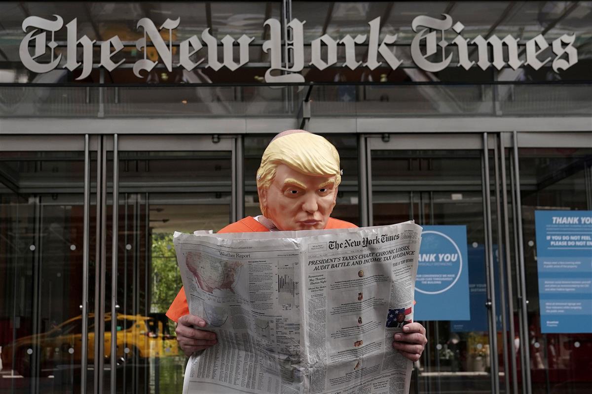 米紙ニューヨーク・タイムズの本社前で、トランプ大統領に模したマスクをかぶり、トランプ氏の税金問題を報じた同紙記事を読む男性。囚人服を着ている=9月28日、ニューヨーク(ロイター)