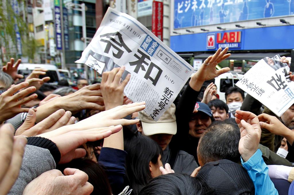新元号「令和」を報じる本紙号外を求め手を伸ばす人々=1日(AP)