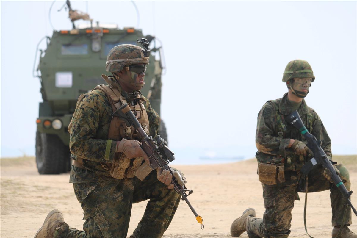 日米合同上陸訓練に参加した陸上自衛隊水陸機動団と米海兵隊の隊員。奥は米軍の高機動ロケット砲システム・HIMARS=2月9日、沖縄県金武町の米軍ブルービーチ訓練場(杉本康士撮影)