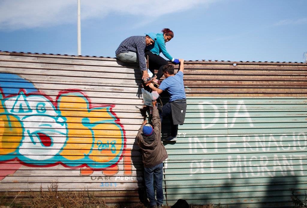 壁を乗り越えて米国への不法入国を試みるホンジュラスからの移民希望者＝１２日、メキシコ・ティフアナ（ロイター）