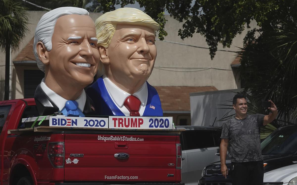 トランプ米大統領(右)とバイデン元副大統領(左)の像の前で記念セルフィ―を撮る通行人=フロリダ州(AP)